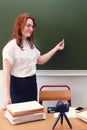 A cute teacher stands in the classroom and writes in chalk on the blackboard. Online education at school and recording video Royalty Free Stock Photo