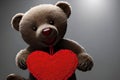 A cute teddy bear holds a red heart