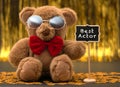 Cute teddy bear with red bow and sunglasses. Little chalkboard with `Best Actor` written whit white chalk