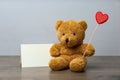 Cute teddy bear with red heart and blank card on wooden table. Valentine`s day celebration Royalty Free Stock Photo