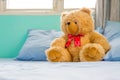 Cute teddy bear sit on the bed in the bedroom with blue pillow. Royalty Free Stock Photo