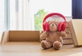 Cute teddy bear wearing red headphone learning stack book