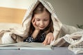 Cute teen child girl lying and reading book on bed under the blanket Royalty Free Stock Photo