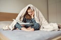 Cute teen child girl lying and reading book on bed under the blanket Royalty Free Stock Photo