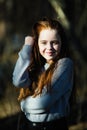 Cute happy teen girl with long bright red hair posing for camera outdoors