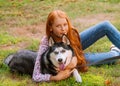 Cute teen girl with red long hair walks with her husky breed dog in the autumn park. Children and dogs. Royalty Free Stock Photo