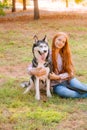 Cute teen girl with red long hair walks with her husky breed dog in the autumn park. Children and dogs. Royalty Free Stock Photo