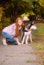 Cute teen girl with red long hair walks with her husky breed dog in the autumn park. Children and dogs.