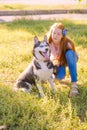 Cute teen girl with red long hair walks with her husky breed dog in the autumn park. Children and dogs.