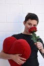 Cute teenage  boy with  a heart shaped pillow and red rose Royalty Free Stock Photo