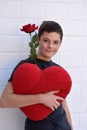 Cute teenage boy with a heart shaped pillow and red rose Royalty Free Stock Photo