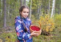 Cute teenage caucasian girl is holding a wicker basket full of red ripe wild lingonberry in northern forest Royalty Free Stock Photo