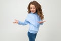 Cute teenage girl in a blue hoodie indignant waving hands on a light gray background