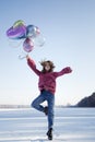 Cute teenage girl, holding many colorful balloons in her hands, jumping up on the snowy ground Royalty Free Stock Photo