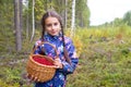 Cute teenage girl is holding a wicker basket full of red ripe wild lingonberry in northern autumn forest