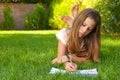 Cute teenage girl lies on the grass and draws