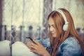 Cute teenage girl listening to music with headphones while holding mobile phone and typing message while relaxing at home Royalty Free Stock Photo