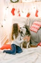 A cute teenage girl with long dark curly hair in a white pullover in a room with a Christmas decor with a large Malamute.