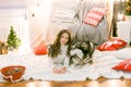 A cute teenage girl with long dark curly hair in a white pullover in a room with a Christmas decor with a large Malamute.