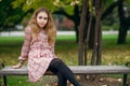 A cute teenage girl with lush hair in a beautiful plaid dress sits on a park bench Royalty Free Stock Photo