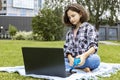 A cute teenage girl sitting on the grass and working on a laptop. A schoolgirl watches an Internet class and studies remotely. The