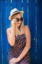 Cute teenage hipster girl smiling in straw hat, dress and sunglasses outdoor over blue wooden background. Royalty Free Stock Photo
