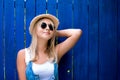Cute teenage hipster girl smiling in straw hat and sunglasses outdoor over blue wooden background. Royalty Free Stock Photo