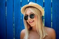 Cute teenage hipster girl smiling in straw hat and sunglasses outdoor over blue wooden background. Royalty Free Stock Photo