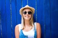 Cute teenage hipster girl with toothy smile in straw hat and sunglasses outdoor over blue wooden background. Royalty Free Stock Photo