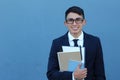 Cute teenager boy in formal high school uniform holding notebooks smiling with copy space wearing glasses