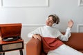 Cute teenager boy wearing earphones listening music and having fun, chilling on sofa near wooden turntable with vinyl record Royalty Free Stock Photo