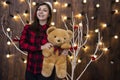 Cute teenager girl holds teddy bear in decorated interior with with Christmas garland yellow lamps illumination on wall background Royalty Free Stock Photo