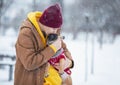 Cute teenager holding french bulldog puppy in his hands and kissing it outdoor on a snow background. Royalty Free Stock Photo