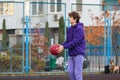 Cute teenager in violet hoodie playing basketball. Young boy with ball learning dribble and shooting on the city court. Hobby Royalty Free Stock Photo