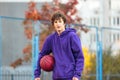 Cute teenager in violet hoodie playing basketball. Young boy with ball learning dribble and shooting on the city court. Hobby Royalty Free Stock Photo