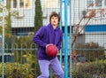 Cute teenager in violet hoodie playing basketball. Young boy with ball learning dribble and shooting on the city court. Hobby Royalty Free Stock Photo