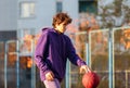 Cute teenager in violet hoodie playing basketball. Young boy with ball learning dribble and shooting on the city court. Hobby Royalty Free Stock Photo