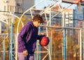 Cute teenager in violet hoodie playing basketball. Young boy with ball learning dribble and shooting on the city court. Hobby Royalty Free Stock Photo
