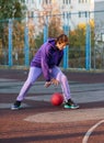 Cute teenager in violet hoodie playing basketball. Young boy with ball learning dribble and shooting on the city court. Hobby Royalty Free Stock Photo