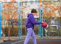 Cute teenager in violet hoodie playing basketball. Young boy with ball learning dribble and shooting on the city court. Hobby Royalty Free Stock Photo