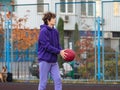 Cute teenager in violet hoodie playing basketball. Young boy with ball learning dribble and shooting on the city court. Hobby Royalty Free Stock Photo