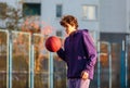 Cute teenager in violet hoodie playing basketball. Young boy with ball learning dribble and shooting on the city court. Hobby Royalty Free Stock Photo