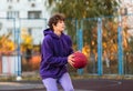 Cute teenager in violet hoodie playing basketball. Young boy with ball learning dribble and shooting on the city court. Hobby Royalty Free Stock Photo