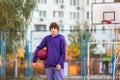 Cute teenager in violet hoodie playing basketball. Young boy with ball learning dribble and shooting on the city court. Hobby Royalty Free Stock Photo