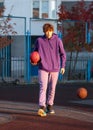 Cute teenager in violet hoodie playing basketball. Young boy with ball learning dribble and shooting on the city court. Hobby Royalty Free Stock Photo