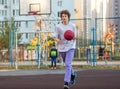 Cute teenager in a white t-shirt playing basketball outside. Young boy with ball learning dribble and shooting on the city court Royalty Free Stock Photo