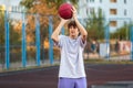 Cute teenager in a white t-shirt playing basketball outside. Young boy with ball learning dribble and shooting on the city court Royalty Free Stock Photo