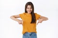 Cute, tender gorgeous brunette female in yellow t-shirt, looking and pointing up, standing amused and wondered, observe