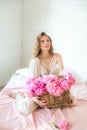 Cute tender young girl with blond hair in white clothes and lace underwear surrounded by pink peonies on the bed Royalty Free Stock Photo