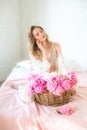 Cute tender young girl with blond hair in white clothes and lace underwear surrounded by pink peonies on the bed Royalty Free Stock Photo